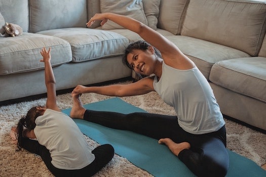 woman doing strethces or yoga in living room having fun with daughter