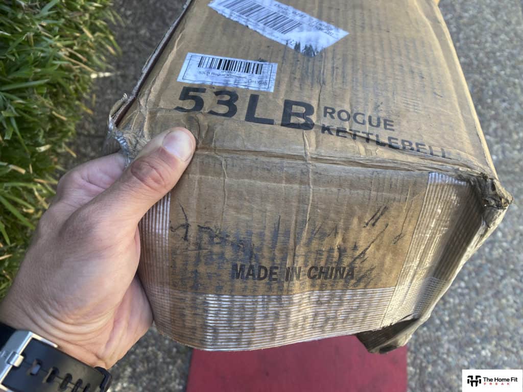 Man's hand holding a Rogue kettlebell box that says "Made in China"