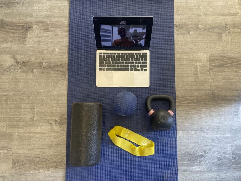 A computer on a video call, a foam roller, an exercise band, and a kettlebell. All on a yoga mat.
